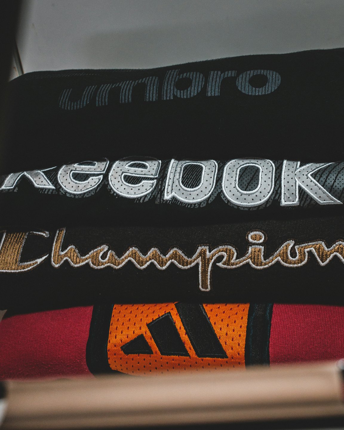 Folded sportswear items with brand logos stacked on a shelf.