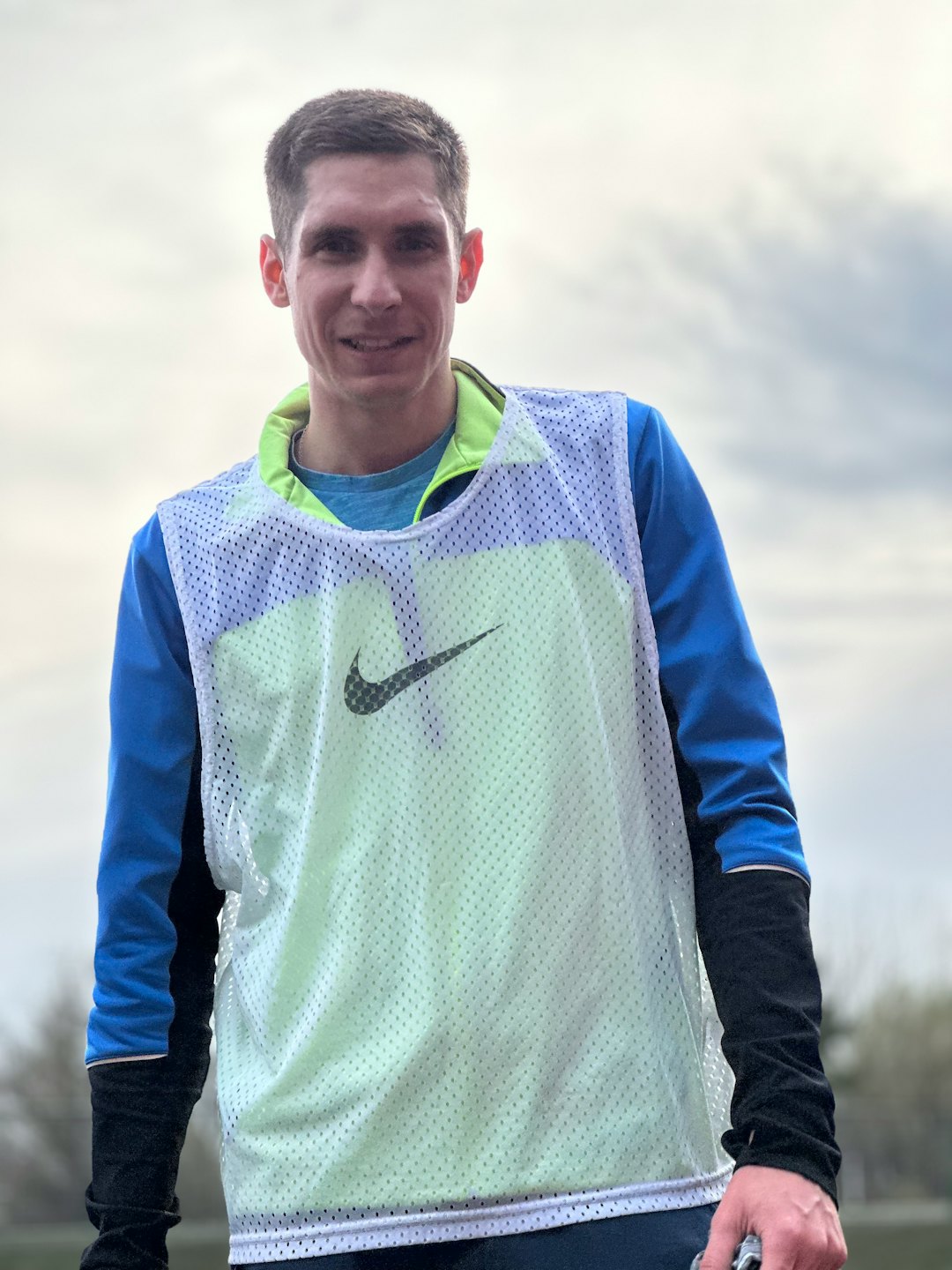 A man in athletic gear smiles outdoors.