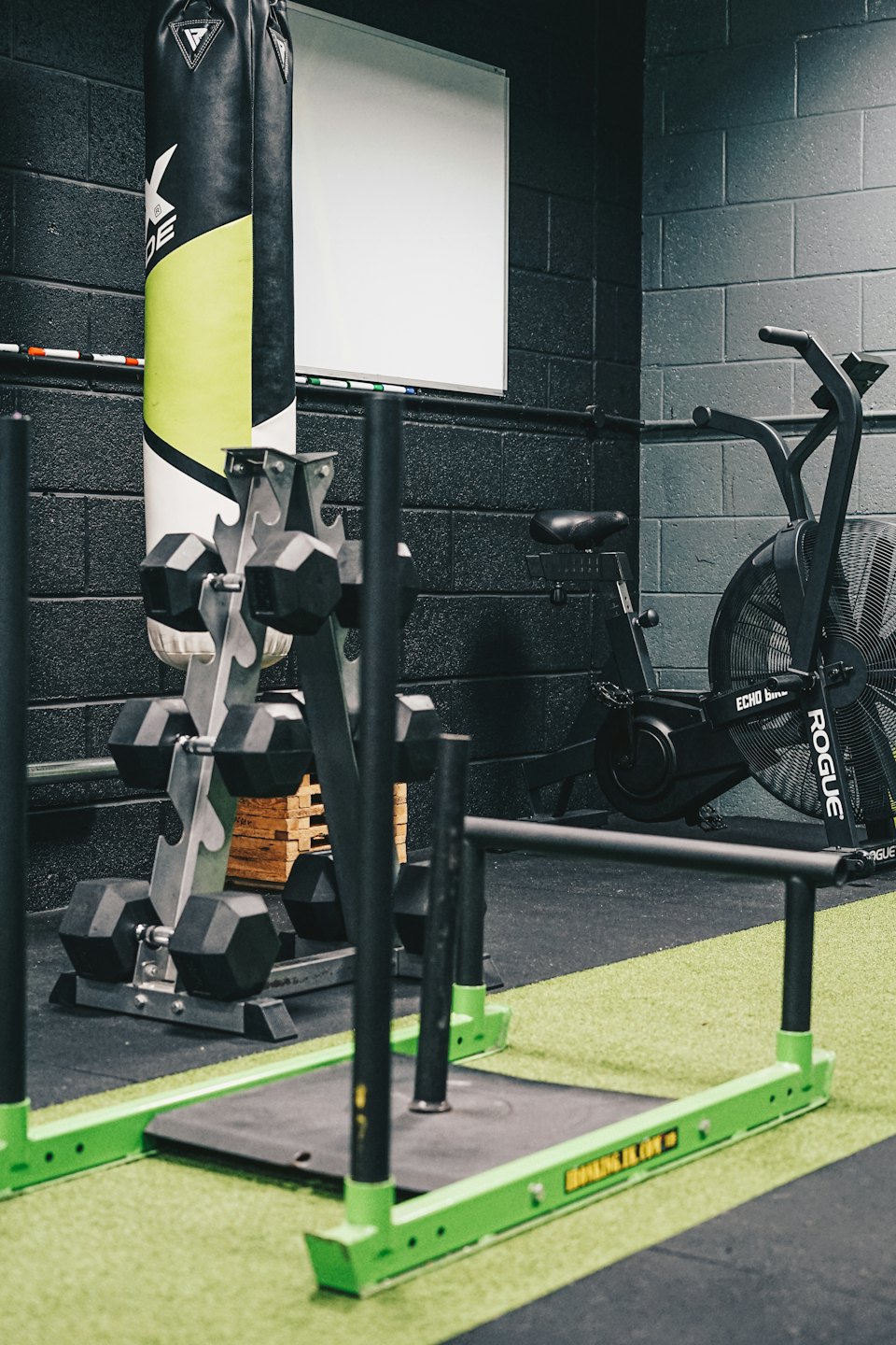 Gym equipment including a sled, dumbbells, punching bag, and air bike.